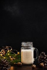 Eggnog traditional Christmas alcoholic drink with cinnamon and nutmeg. Eggnog in a jar and a bottle. Winter holidays mood. Dark background. Copyspace. Vertical