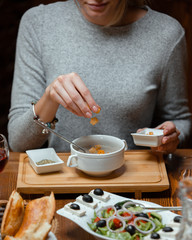 Woman putting bread stuffing cubes in her mushroom soup served with greek salad