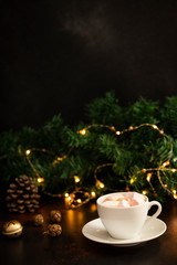 Warm cocoa drink with marshmallows. Christmas and New Year drink. Christmas Eve mood. Christmas lights and decorations. Winter holidays concept. Dark background. Vertical. Copyspace