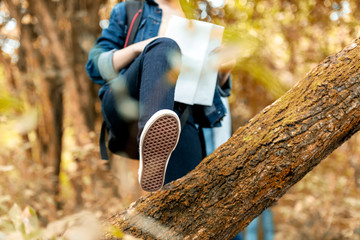 Close up shoe crossed over the tree.   Asian traveler with backpack adventure holding map to find...