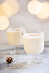 Eggnog traditional homemade Christmas and New Year drink with cinnamon and nutmeg. Winter holidays mood. Christmas lights. Light background. Selective focus. Vertical