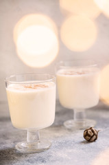 Eggnog traditional homemade Christmas and New Year drink with cinnamon and nutmeg. Winter holidays mood. Christmas lights. Light background. Selective focus. Vertical