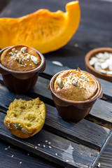 Pumpkin muffins on a dark wooden and half a broken cupcake and a slice of pumpkin in the background