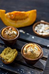 Pumpkin muffins on a dark wooden and half a broken cupcake and a slice of pumpkin in the background