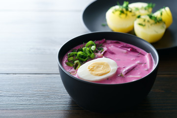 Lithuanian Saltibarsciai (Cold Beet Soup) with hard boiled egg and potatoes, seasoned with spring onions and dill. Dark wooden table, high resolution