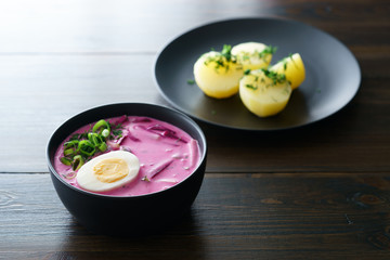 Lithuanian Saltibarsciai (Cold Beet Soup) with hard boiled egg and potatoes, seasoned with spring onions and dill. Dark wooden table, high resolution