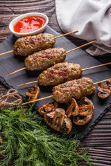 Shish kebab on the skewers with sauce, grilled mushrooms on rustic table