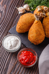 fried chicken leg in batter, red and white sauce on a dark surface
