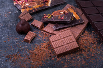 Pieces of dark and milk chocolate and candies on a dark background.