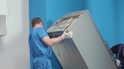 Men in uniform bring a fridge at the kitchen.