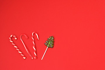 Christmas holiday lollipop candy decorative lying on the red background flat lay top view. Festive decor for xmas and new year winter holidays. Sweet fir-tree and striped red and white candies