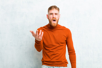 young red head man wearing turtle neck looking angry, annoyed and frustrated screaming wtf or...