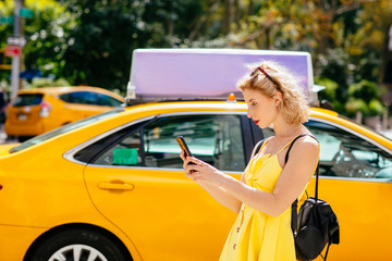 Young woman with cell phone standing in front of yellow taxis in New York, New York City