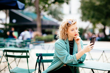Fototapeta na wymiar Portrait of a young blonde woman sitting outside reading and holding cell phone
