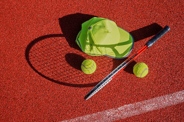 Tennis racket, peaked cap and balls on court