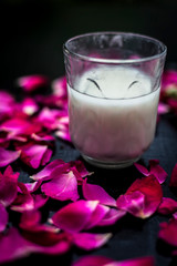 Fresh raw milk in a glass on a black surface along with some rose petals spread. Vertical shot.