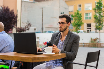 Obraz premium Young businessman is working in a bar terrace with his laptop and smartphone