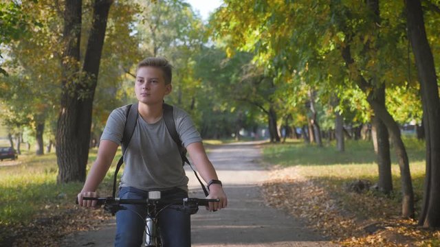 Teenage boy rides bike in city park at sunny day. Healthy lifestyle concept.