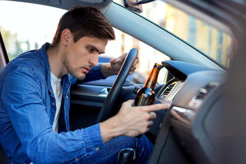 Obraz premium Młody brunet pije piwo za kierownicą samochodu. Pijany kierowca jedzie w samochodzie. Mężczyzna łamie przepisy ruchu drogowego. Koncepcja jazdy po alkoholu. Śmiertelne niebezpieczeństwo na trasie współczesnego miasta.