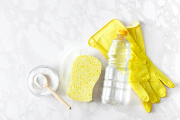 Baking soda, a bottle of vinegar, rubber gloves on a marble surface. Top view.