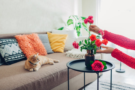 Woman puts flowers roses in vase on table. Housewife taking care of coziness in apartment. Interior and decor