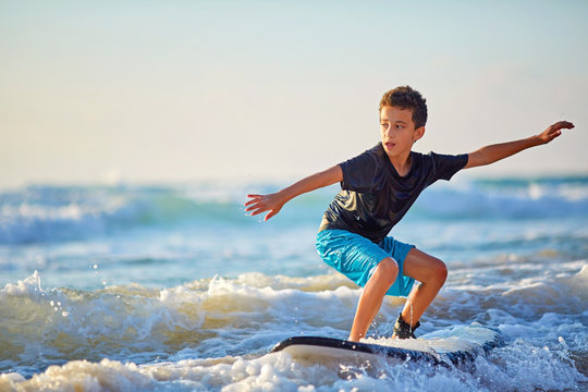 Skilled teenager riding surfboard and balancing a long wavy sea.