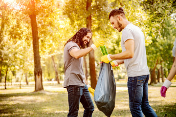 Team of friends cleaning up the park by collecting litter into plastic bags