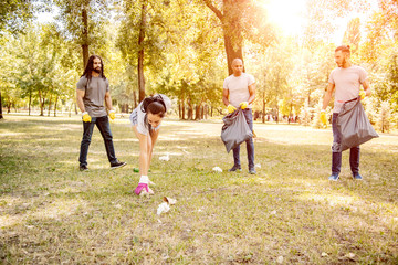 Team of friends cleaning up the park by collecting litter into plastic bags