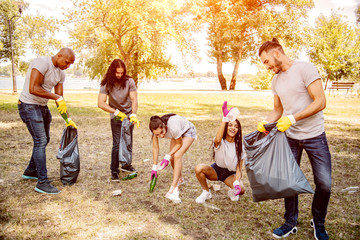 Team of friends cleaning up the park by collecting litter into plastic bags