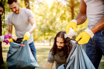 Team of friends cleaning up the park by collecting litter into plastic bags