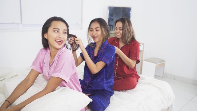 Group of beautiful teenage girls sitting on the bed while tying the friends hair and wearing pajama. Shot in 4k resolution