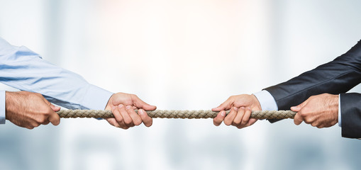 Tug of war, two businessman pulling a rope in opposite directions over defocused background with copy space - obrazy, fototapety, plakaty