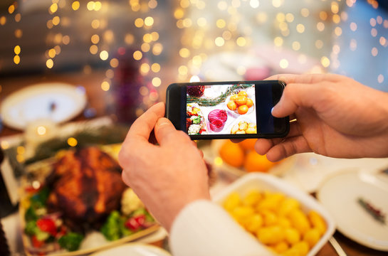 technology, eating and holidays concept - close up of male hands photographing food by smartphone at christmas dinner