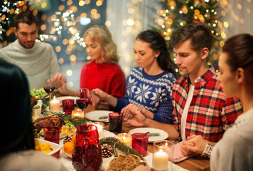 holidays and celebration concept - friends holding hands and praying while having christmas dinner...