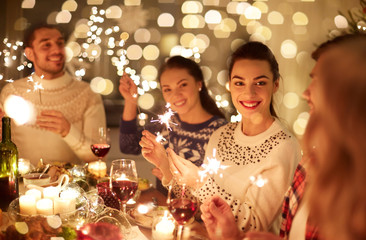 winter holidays and people concept - happy friends with sparklers celebrating christmas at home...