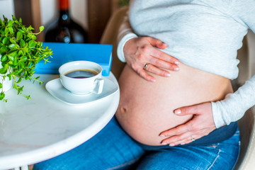 Young beautiful pregnant girl drinking coffee in her home during daytime