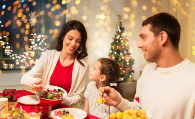 holidays, family and celebration concept - happy mother, father and little daughter having christmas dinner at home