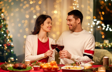 holidays, family and celebration concept - happy couple having christmas dinner at home and drinking red wine and clinking glasses