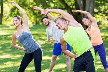 fitness, sport and healthy lifestyle concept - group of happy people exercising at summer park