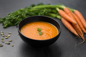 food, new nordic cuisine, culinary and cooking concept - close up of vegetable pumpkin cream soup with mint leaf in bowl, carrot and seeds on stone table