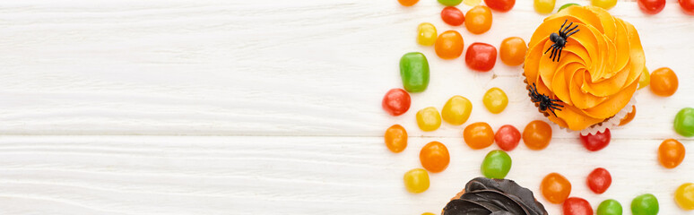 panoramic shot of colorful bonbons and cupcakes on white wooden table, Halloween treat