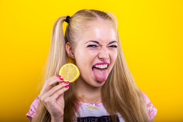 Naughty blonde with lemon slice makes a sour face facial expression isolated against yellow...