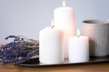 decoration, hygge and cosiness concept - burning white candles, tea in mug and lavender flowers on tray on table