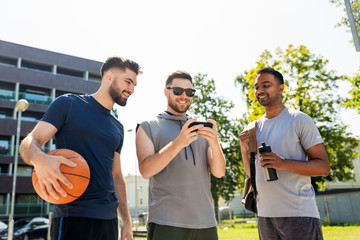 sport, leisure games and male friendship concept - group of men or friends with smartphone at outdoor basketball playground