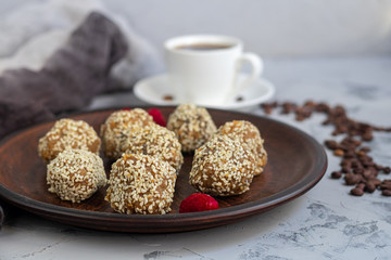Fototapeta na wymiar On a brown clay plate are Indian sweets Lada. They are sprinkled with sesame seeds. In the background is a cup of hot, aromatic coffee. Everything is located on a gray background decorated in granite.