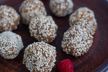 On a brown clay plate are Indian Lada balls. They are sprinkled with sesame seeds. Everything is located on a gray background decorated in granite. 
