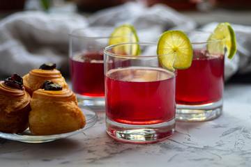Drink from plums and apples in transparent glasses. On a plate are cupcakes with cream filling. Lime slices add acidity and are a decor. 