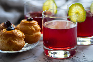 Drink from plums and apples in transparent glasses. On a plate are cupcakes with cream filling. Lime slices add acidity and are a decor. 