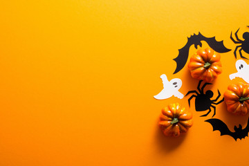 Happy halloween holiday concept. Halloween decorations, spiders, bats, ghosts, pumpkins on orange background. Halloween party greeting card mockup with copy space. Flat lay, top view, overhead.