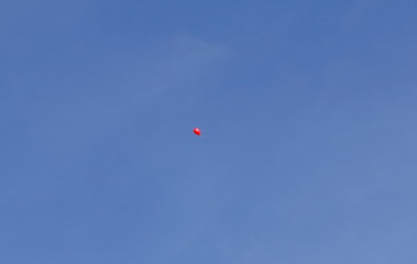 A red balloon rises into the immense blue sky